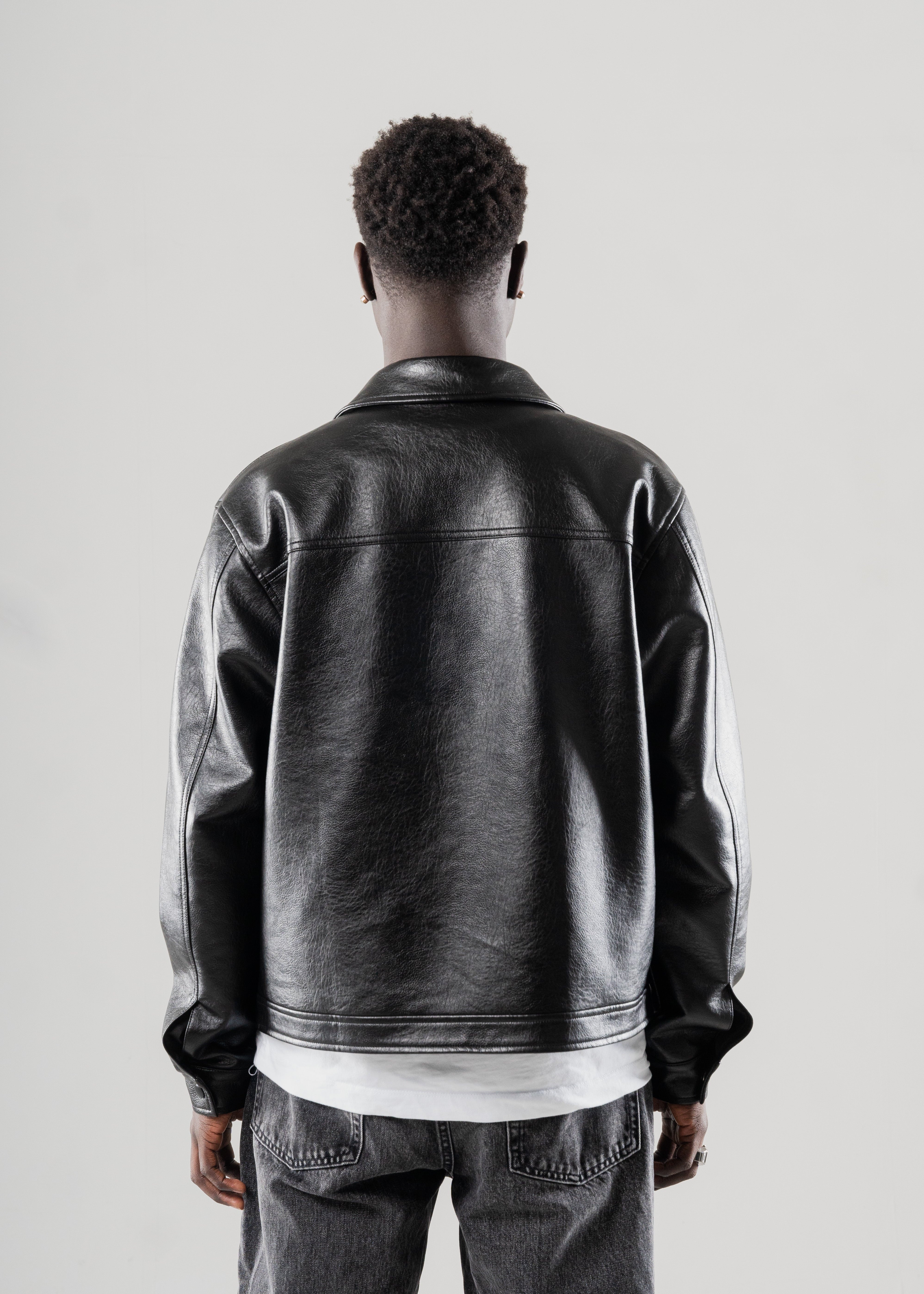 model wearing a Mallacco black vegan leather jacket from behind on a light gray background
